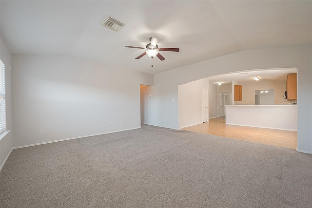 unfurnished living room featuring light carpet, visible vents, arched walkways, baseboards, and ceiling fan