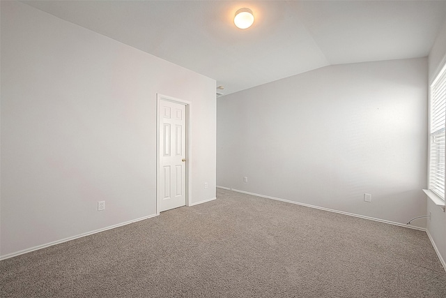 carpeted spare room featuring lofted ceiling and baseboards