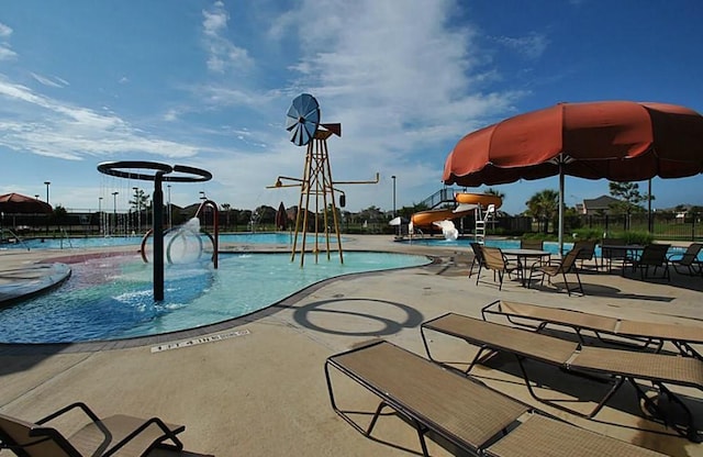 pool featuring a water slide, a patio area, a water play area, and fence