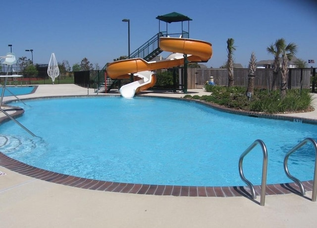 community pool with playground community, a water slide, and fence