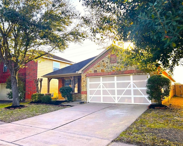 traditional-style home with brick siding, fence, a garage, stone siding, and driveway