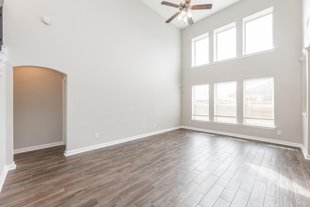 empty room with baseboards, ceiling fan, arched walkways, high vaulted ceiling, and dark wood-style flooring