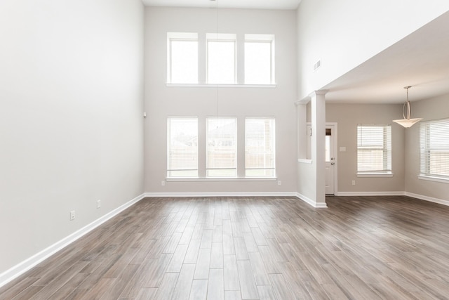 unfurnished living room featuring visible vents, decorative columns, baseboards, and wood finished floors