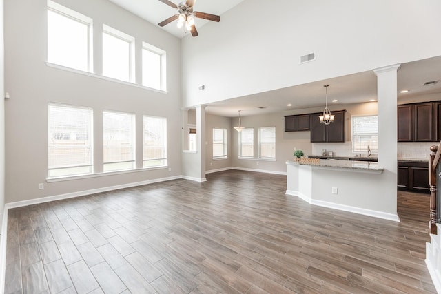 unfurnished living room with ceiling fan with notable chandelier, decorative columns, wood finished floors, and visible vents