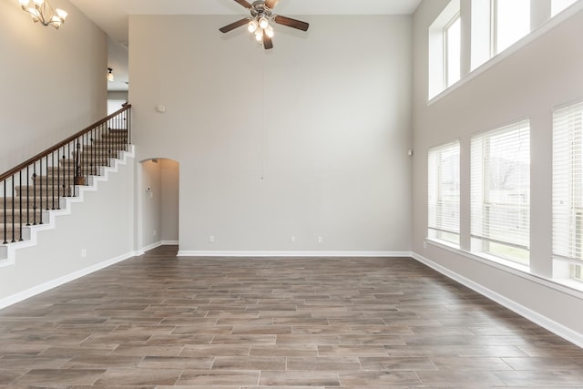 unfurnished living room with arched walkways, ceiling fan, baseboards, and wood finished floors