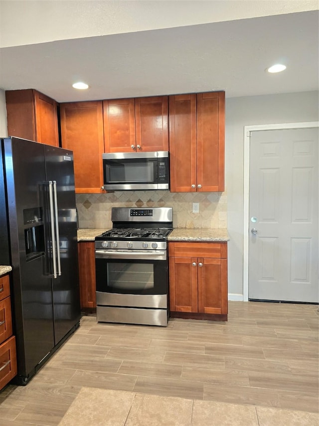 kitchen with wood finish floors, stainless steel appliances, recessed lighting, backsplash, and light stone countertops