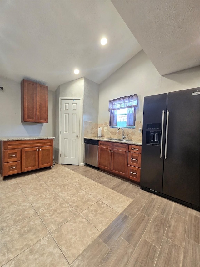 kitchen with light stone counters, black refrigerator with ice dispenser, vaulted ceiling, a sink, and dishwasher