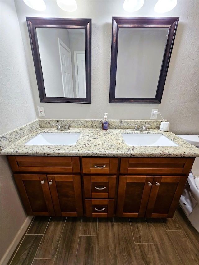 bathroom with double vanity, toilet, a sink, and wood finish floors