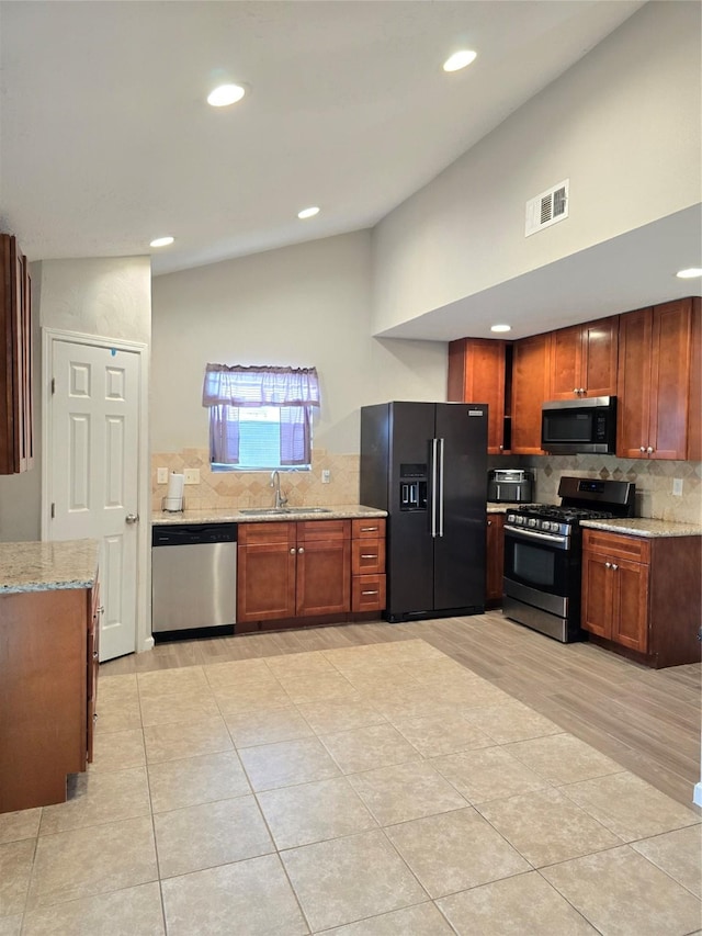 kitchen featuring visible vents, light stone counters, vaulted ceiling, stainless steel appliances, and a sink