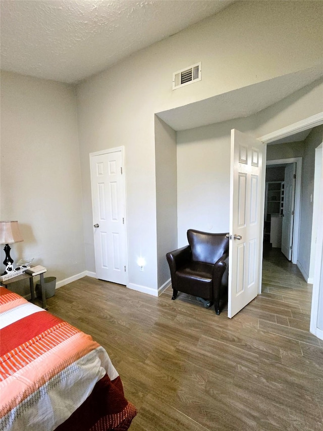 bedroom with a textured ceiling, wood finished floors, visible vents, and baseboards