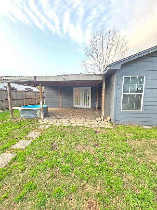 rear view of house with a wooden deck, french doors, fence, a yard, and a pool