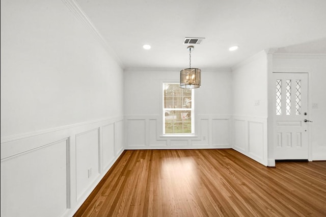 unfurnished dining area featuring visible vents, ornamental molding, wood finished floors, a decorative wall, and recessed lighting