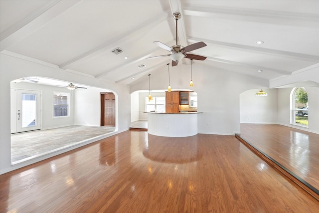 unfurnished living room with arched walkways, ceiling fan, lofted ceiling with beams, wood finished floors, and visible vents