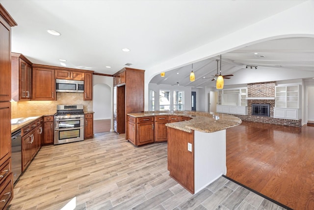 kitchen featuring appliances with stainless steel finishes, vaulted ceiling with beams, light stone countertops, a peninsula, and a brick fireplace