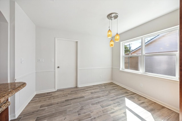 unfurnished dining area with light wood-style floors and a wainscoted wall