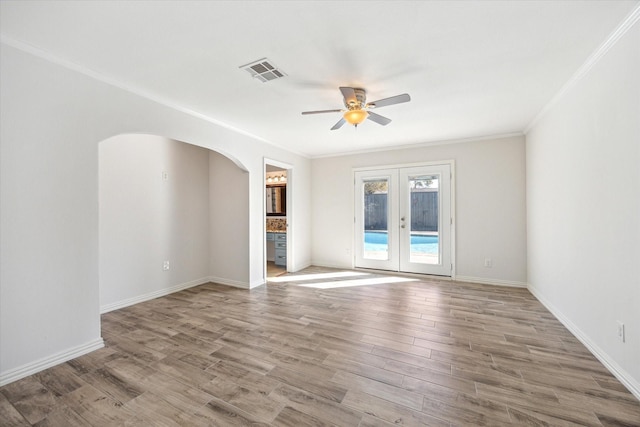 empty room featuring visible vents, arched walkways, ornamental molding, wood finished floors, and french doors