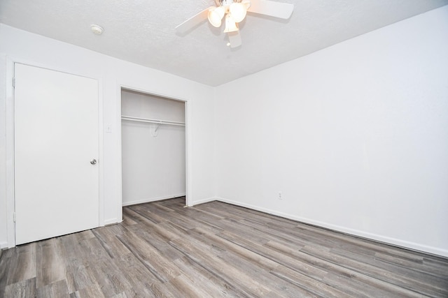 unfurnished bedroom featuring a closet, a ceiling fan, a textured ceiling, wood finished floors, and baseboards