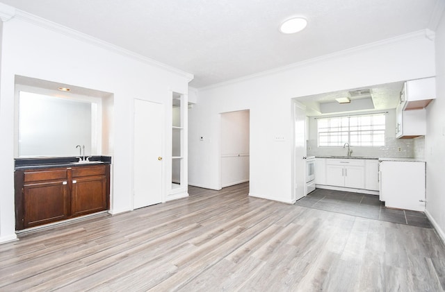 kitchen with light wood-type flooring, crown molding, backsplash, and a sink