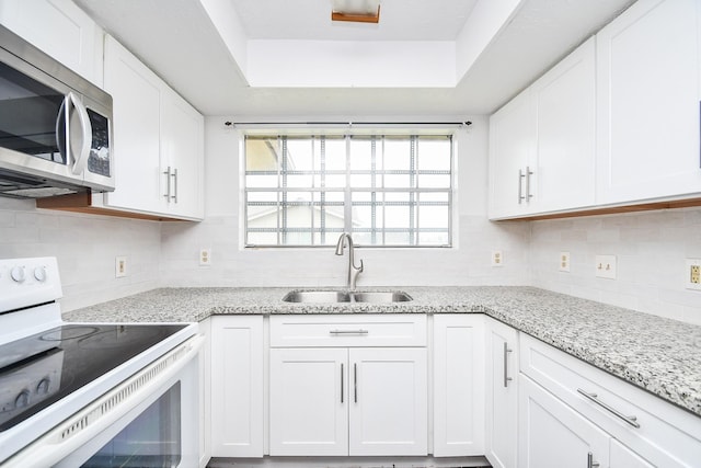 kitchen with a sink, white cabinets, white range with electric stovetop, a tray ceiling, and stainless steel microwave