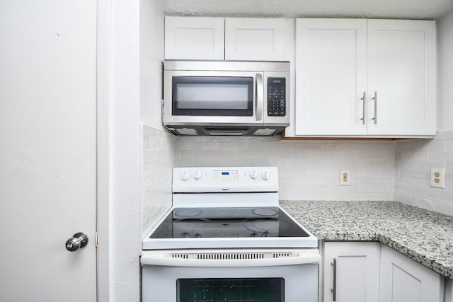 kitchen with light stone counters, white range with electric cooktop, stainless steel microwave, backsplash, and white cabinetry