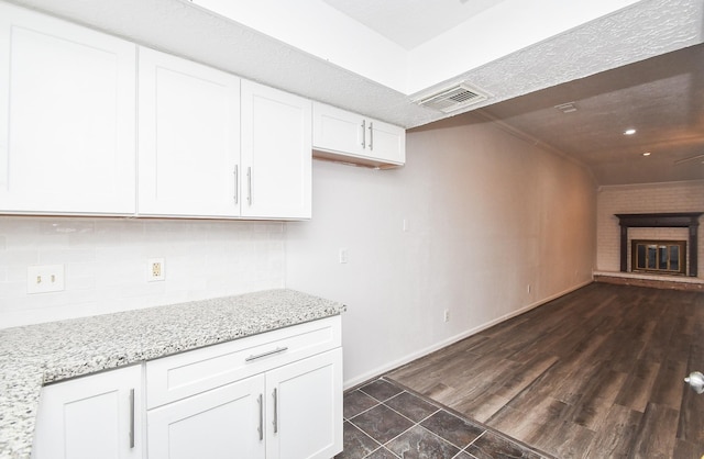 kitchen featuring tasteful backsplash, light stone counters, visible vents, and white cabinetry