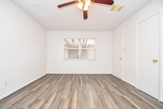 unfurnished room featuring a ceiling fan, visible vents, baseboards, and wood finished floors