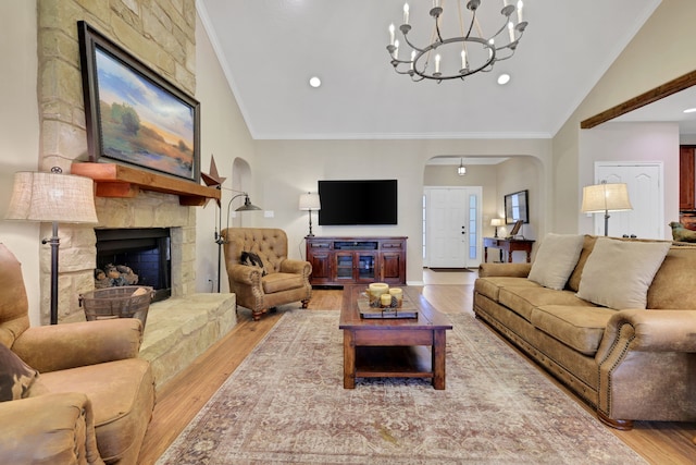 living area featuring light wood-style floors, a fireplace, arched walkways, and crown molding