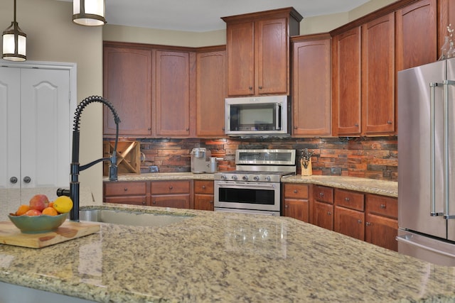 kitchen with appliances with stainless steel finishes, a sink, light stone countertops, pendant lighting, and backsplash