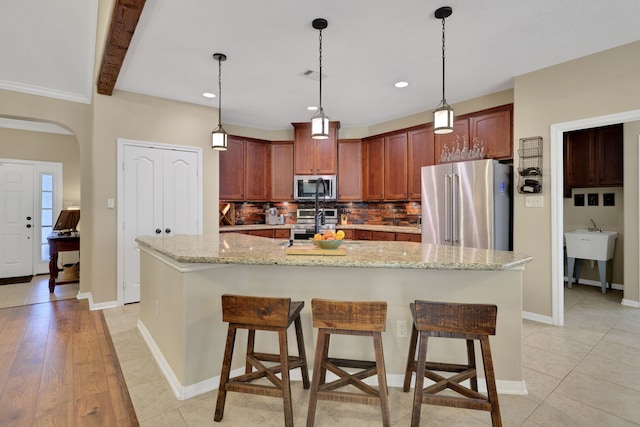 kitchen with arched walkways, a breakfast bar area, stainless steel appliances, visible vents, and tasteful backsplash