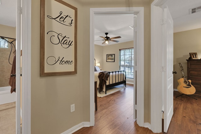 corridor with hardwood / wood-style flooring, visible vents, and baseboards