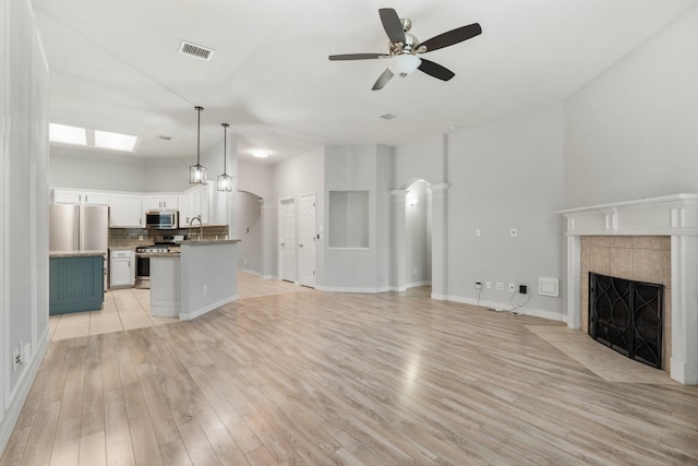 unfurnished living room featuring light wood-style floors, visible vents, arched walkways, and a tiled fireplace