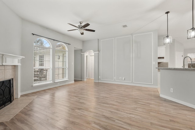 unfurnished living room with a fireplace, light wood finished floors, visible vents, a ceiling fan, and a sink