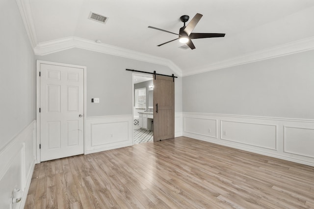 unfurnished bedroom with lofted ceiling, a barn door, light wood-style flooring, visible vents, and ornamental molding