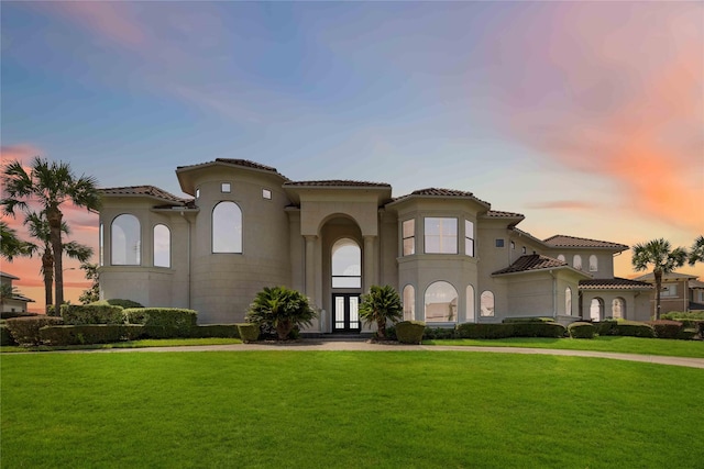 mediterranean / spanish house featuring a tiled roof, a front yard, and stucco siding