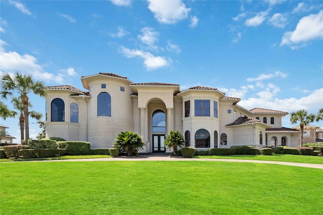 mediterranean / spanish house with a tile roof, a front lawn, french doors, and stucco siding