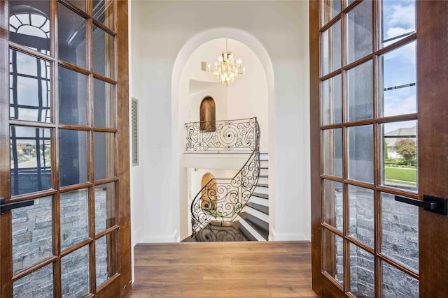 hall with wood finished floors, french doors, arched walkways, baseboards, and a notable chandelier
