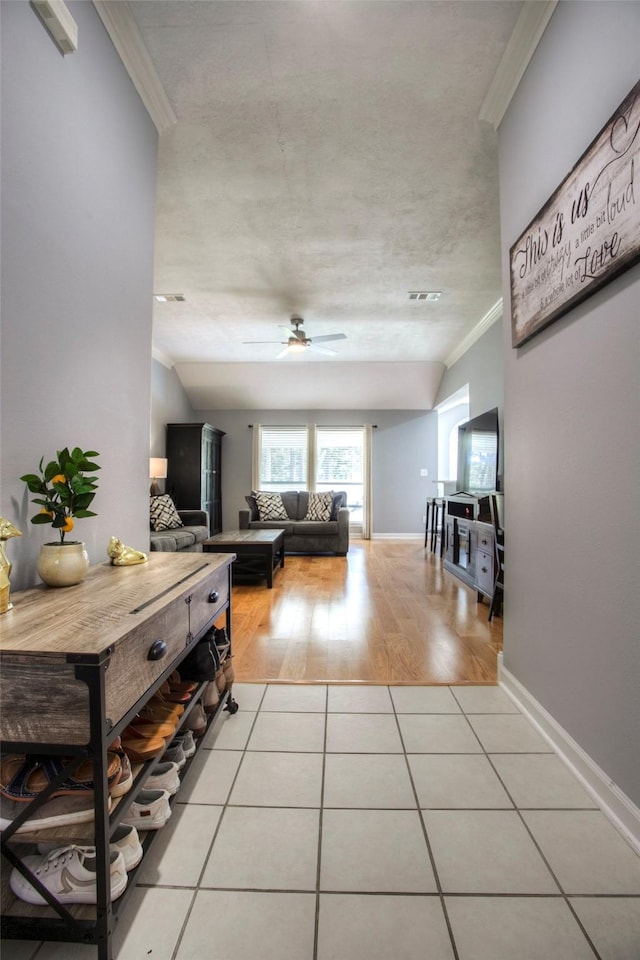 hall with light tile patterned floors, lofted ceiling, visible vents, ornamental molding, and baseboards