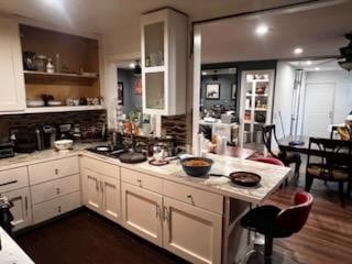 kitchen with dark wood-style floors, a breakfast bar, a peninsula, open shelves, and light countertops