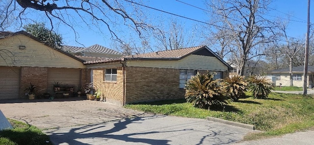 view of side of home with aphalt driveway, a tiled roof, a garage, and brick siding