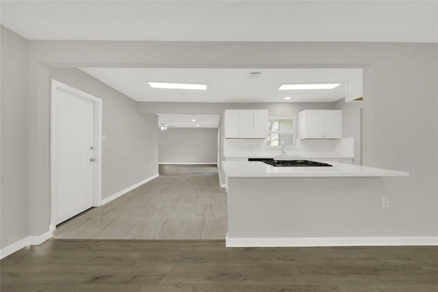 kitchen with a sink, wood finished floors, white cabinetry, baseboards, and light countertops