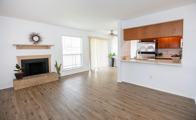 unfurnished living room featuring ceiling fan, a fireplace, a sink, wood finished floors, and baseboards