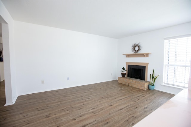 unfurnished living room featuring a brick fireplace, baseboards, and wood finished floors