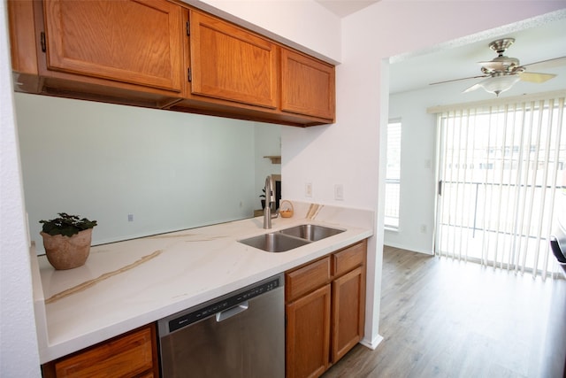 kitchen featuring brown cabinets, stainless steel dishwasher, a ceiling fan, a sink, and wood finished floors