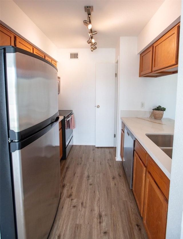 kitchen with stainless steel appliances, visible vents, brown cabinetry, a sink, and wood finished floors