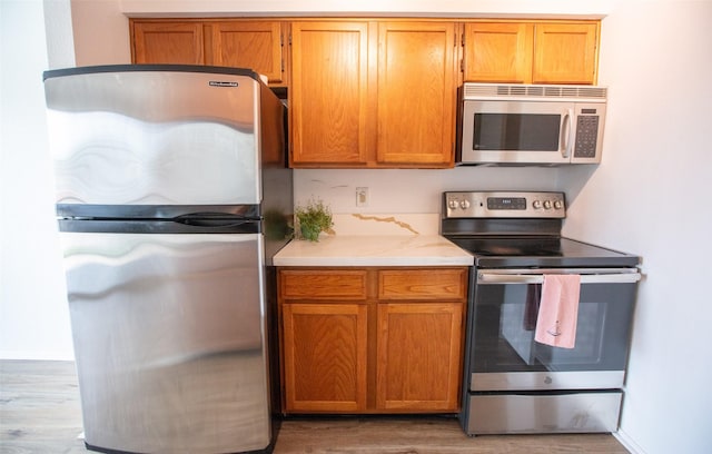 kitchen featuring appliances with stainless steel finishes, brown cabinets, and wood finished floors