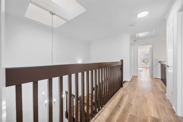 hall featuring light wood-style flooring, a skylight, an upstairs landing, and attic access