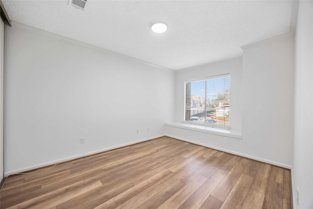 unfurnished room featuring a textured ceiling, wood finished floors, visible vents, baseboards, and ornamental molding