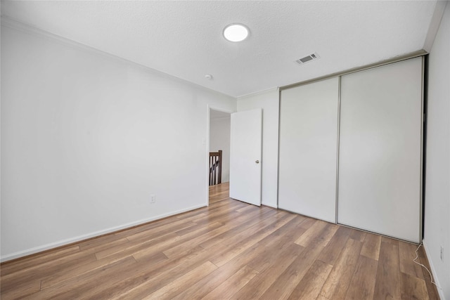 unfurnished bedroom with light wood-style floors, a closet, visible vents, and a textured ceiling