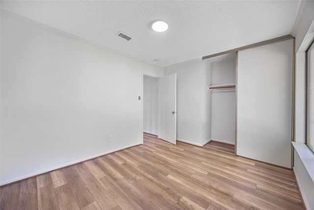 unfurnished bedroom with a closet, visible vents, ornamental molding, a textured ceiling, and wood finished floors