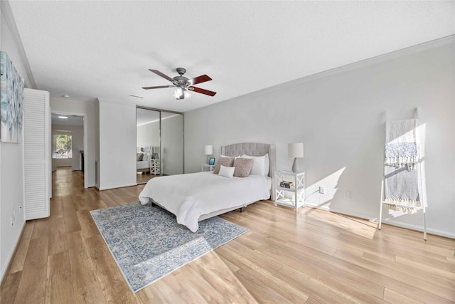 bedroom featuring a ceiling fan, light wood-style flooring, ornamental molding, a textured ceiling, and a closet